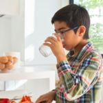 child drinking glass of water at home