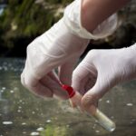 Water hardness test. Hands in gloves collect water sample for titration. Waterfall background.