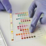 Alkaline water research: Gloved hands compare urine test strip to color chart. Analyzing pH levels.