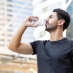 Man drinking bottled water. Concerned about PFAS regulations and NYC drinking water safety. Stay hydrated with clean water.
