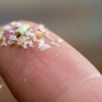 Microplastics on a fingertip. Tiny plastic particles, various colors and shapes. Health risks of ingesting microplastics concept.