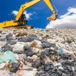 Excavator on landfill. Mercury (Hg) pollution from waste impacts water quality.