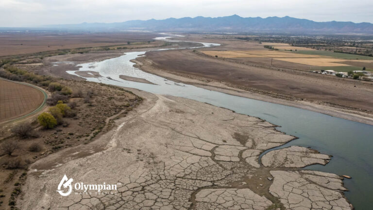 Shrinking Colorado River. Aerial view of drought-stricken riverbed with cracked earth. Mountains in background.