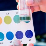 Well water pH test. Comparing water sample to pH color chart. Low pH well water affects plumbing and body.