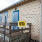 Lead hazard remediation at older well site. Caution sign on fence. Windows and doors covered.