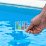 Well water test. Hand holding water testing kit against a blue pool. Home inspection and water quality.