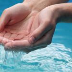 Hands cupping clear well water. Water softeners improve well water quality. Clean, safe drinking water concept.