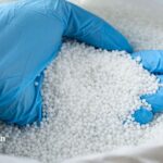 Nitrates in well water. Hand in blue glove holding white nitrate pellets for water testing.