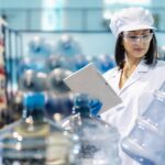 Well water quality testing. Technician inspecting water bottles with a tablet in a lab.